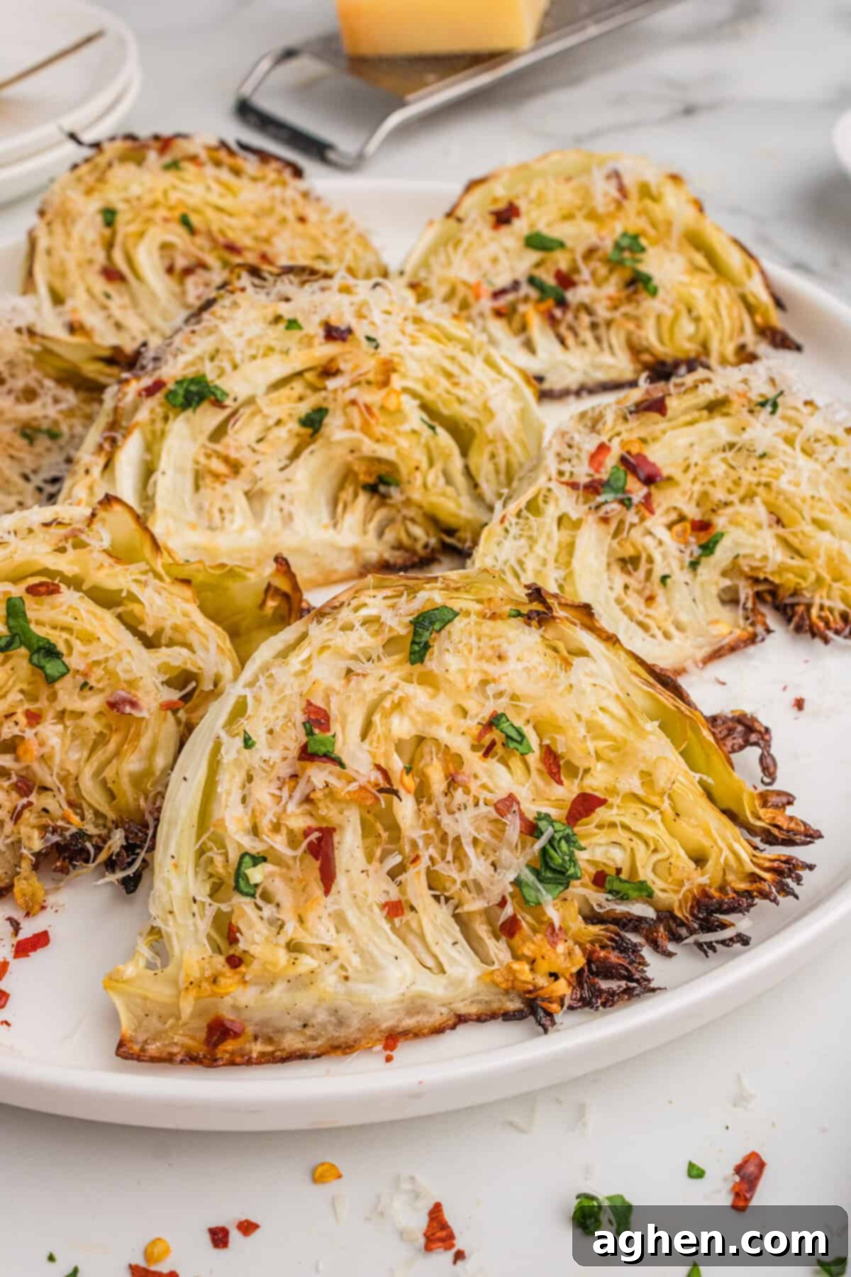 Golden Roasted Cabbage Wedges 2 Roasted cabbage wedges with garlic, Parmesan cheese, and red pepper flakes, served on a white plate.
