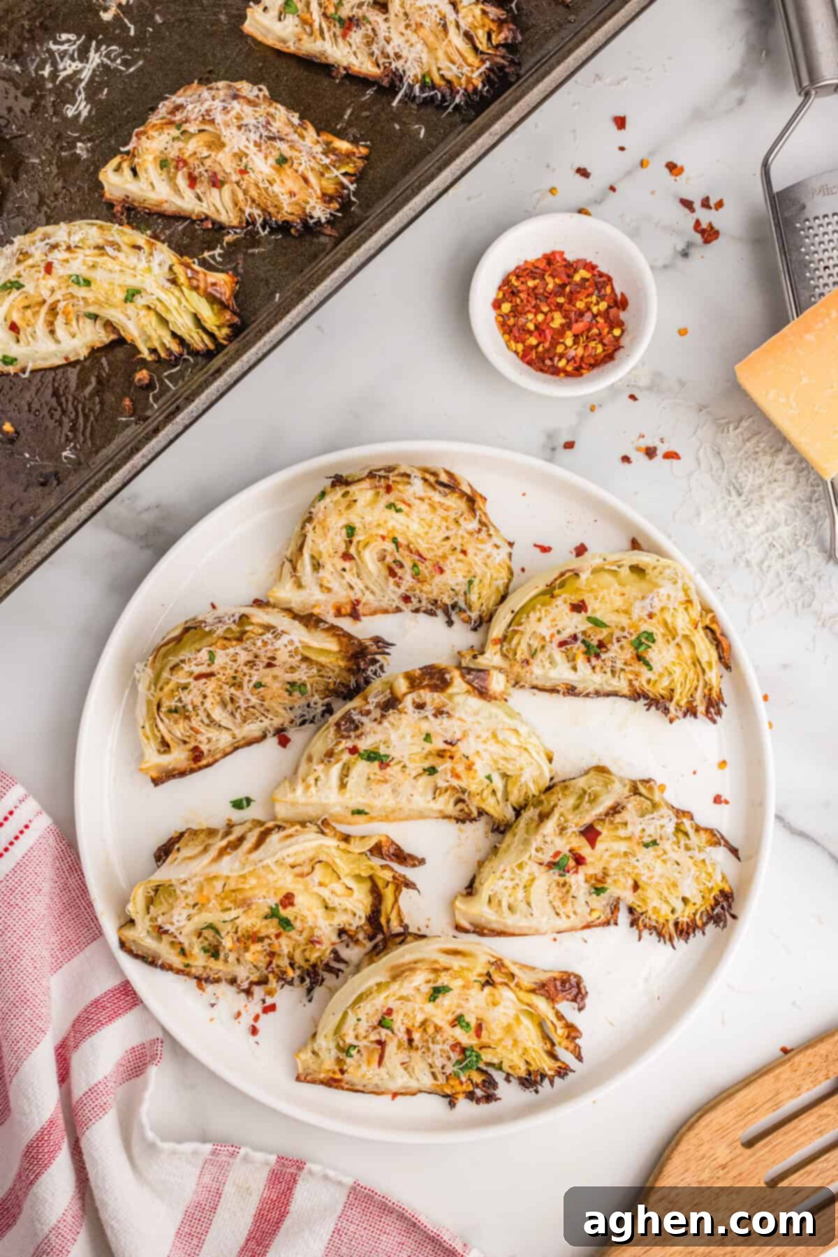 Golden Roasted Cabbage Wedges 9 Roasted garlic parmesan cabbage wedges arranged on a white serving plate and baking sheet, topped with shredded parmesan, parsley, and red pepper flakes.