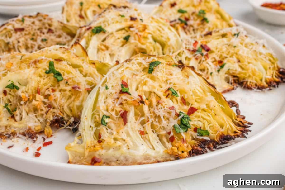Golden Roasted Cabbage Wedges 10 Close-up of roasted garlic parmesan cabbage wedges on a white plate, topped with shredded parmesan, parsley, and red pepper flakes.