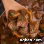 A wooden spoon lifting honey bourbon steak tips garnished with parsley from a slow cooker filled with more steak bites.