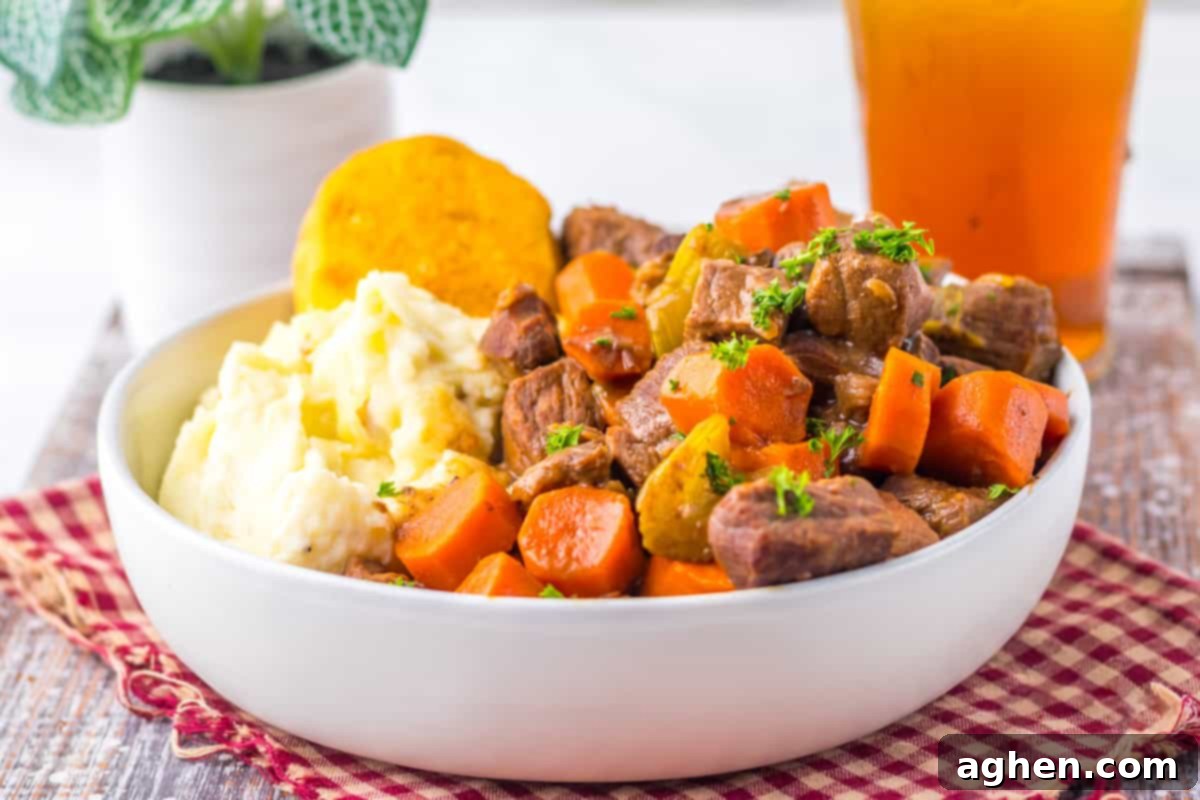 Side view of a bowl of crockpot pot roast, featuring stew beef, sliced carrots, celery, mashed potatoes, and a biscuit.