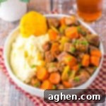 Bowl of crockpot cracker barrel copycat pot roast with carrots, celery, mashed potatoes, and a biscuit.