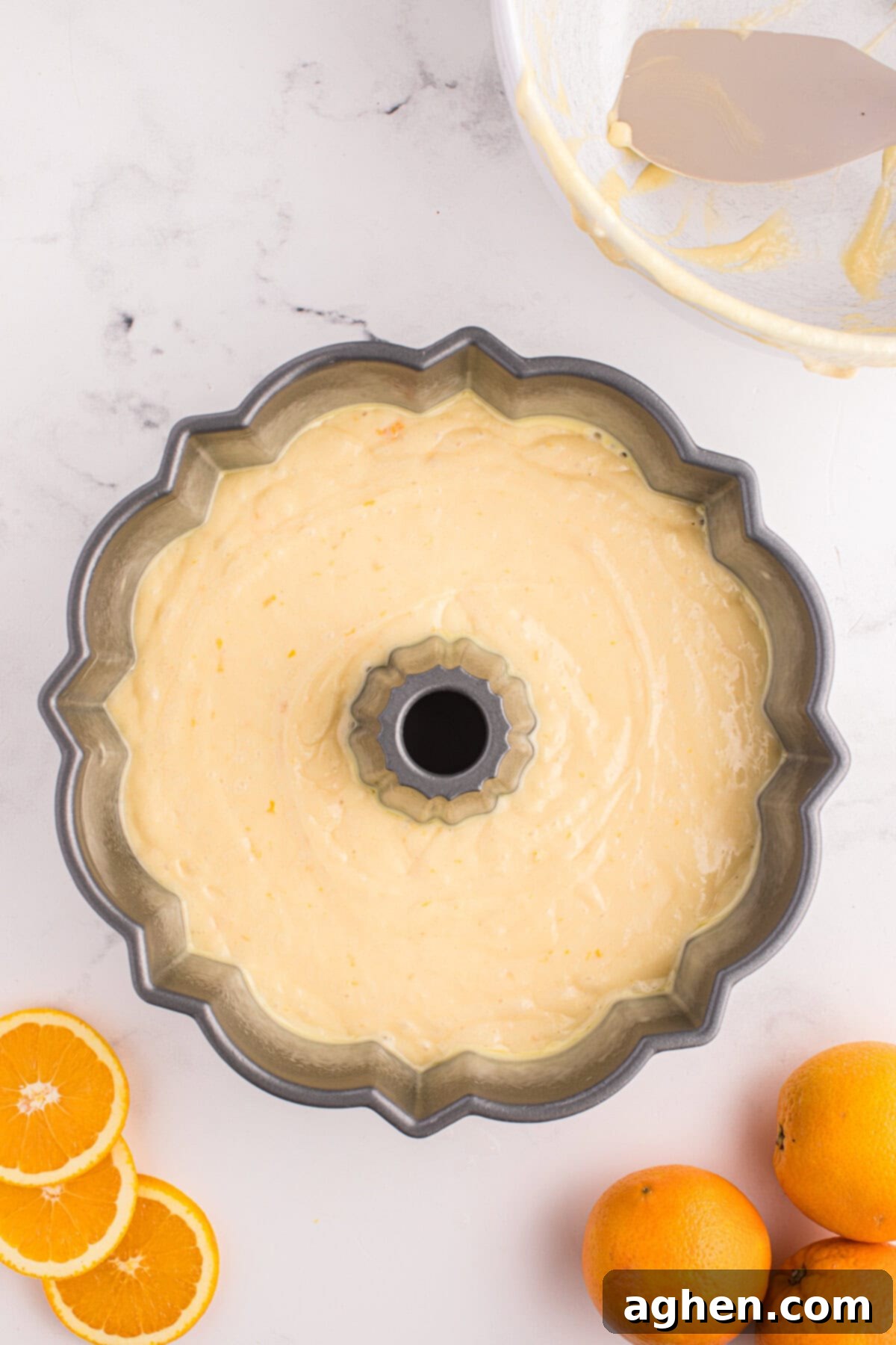 A scalloped-edge Bundt cake pan is filled with light orange batter, ready to bake. The batter is smooth and evenly spread.