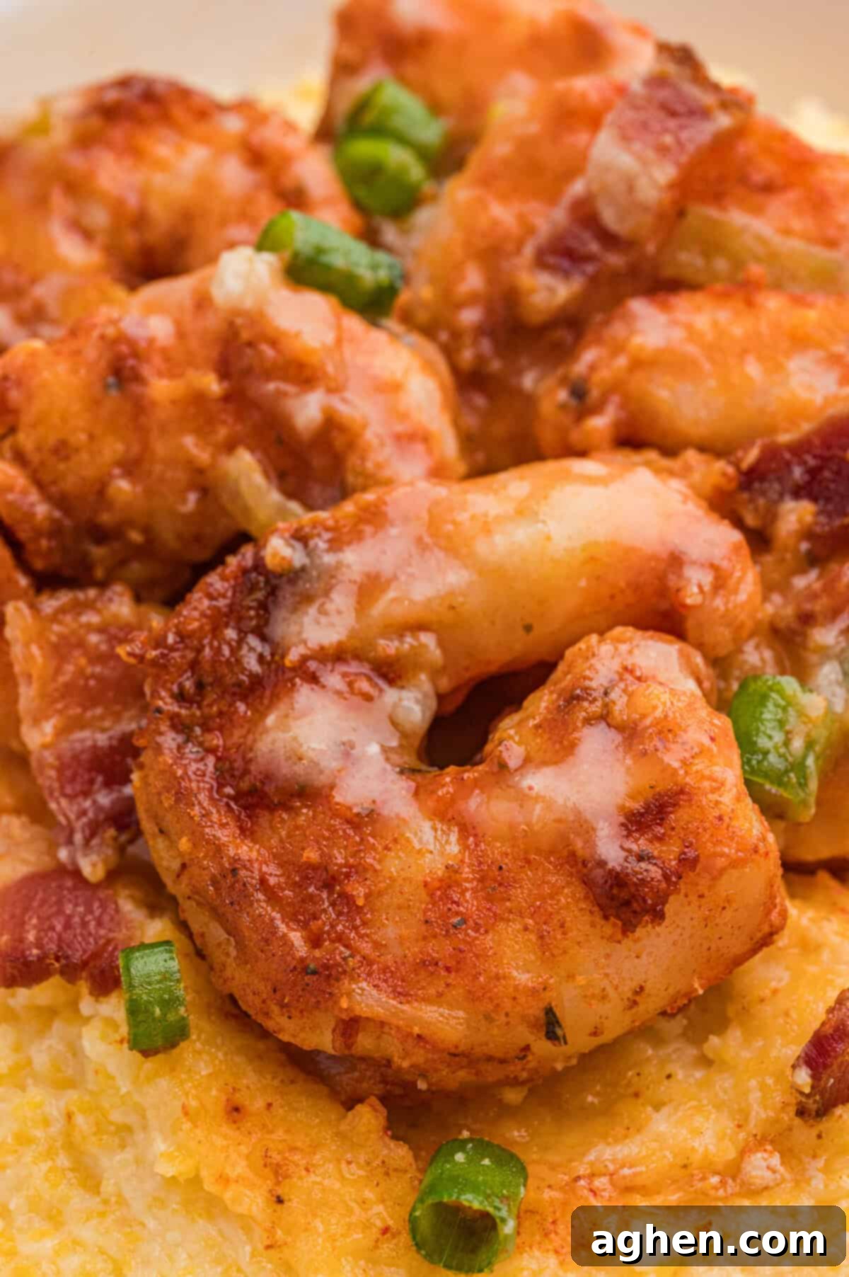 Saucy, seasoned shrimp resting on creamy yellow grits, with visible pieces of green onion and bacon.