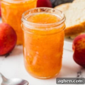 Jars of homemade peach jam with whole peaches, a spoon, and a plate with sliced bread in the background. Peach Jam (No Pectin) Recipe Card Image.