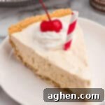 A slice of root beer float pie on a plate, topped with whipped cream, a cherry, and a red-striped paper straw.