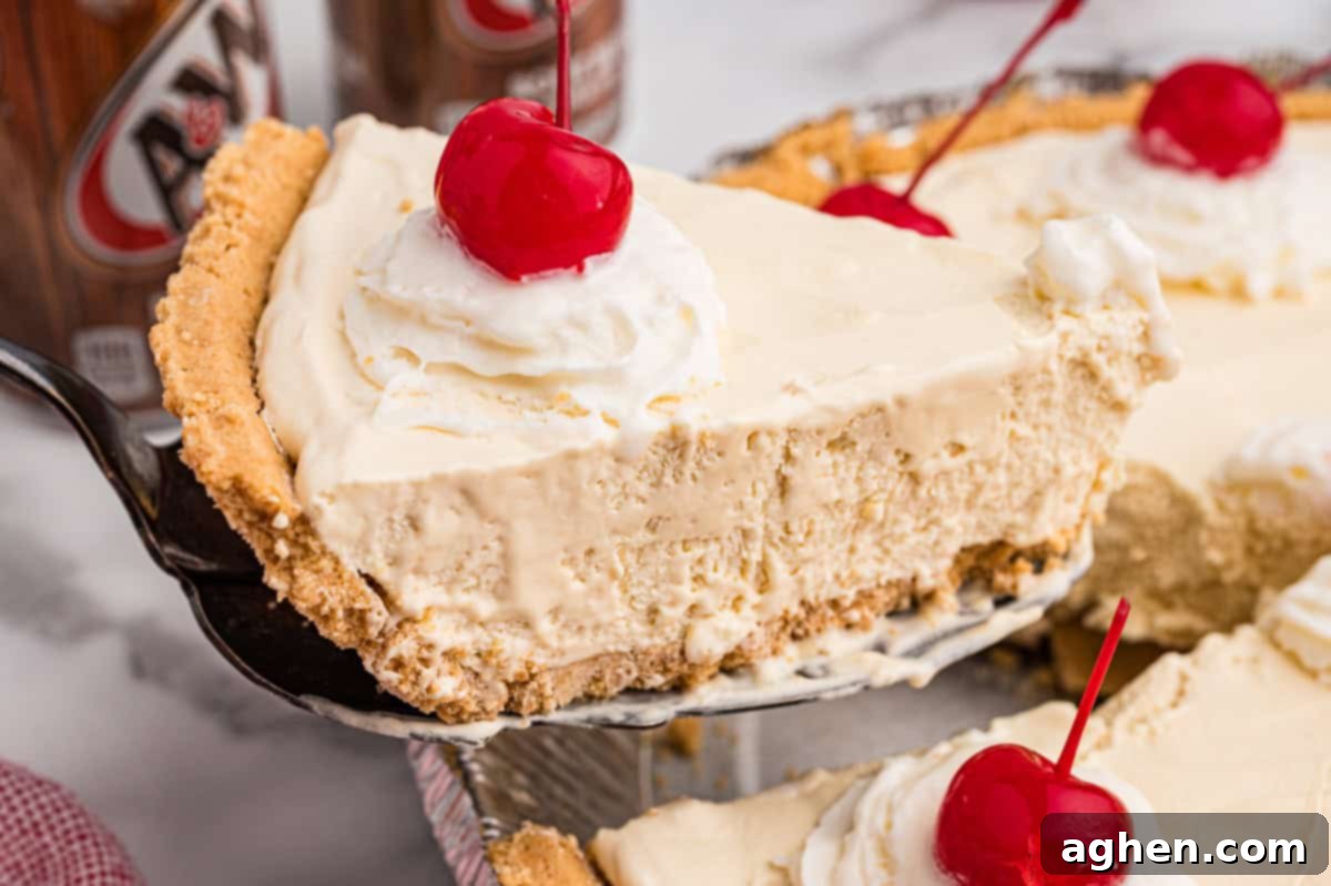 A glorious slice of root beer float pie is being carefully lifted out of its pan with a pie server, highlighting its creamy filling, perfectly formed graham cracker crust, and the inviting topping of whipped cream and a single maraschino cherry.