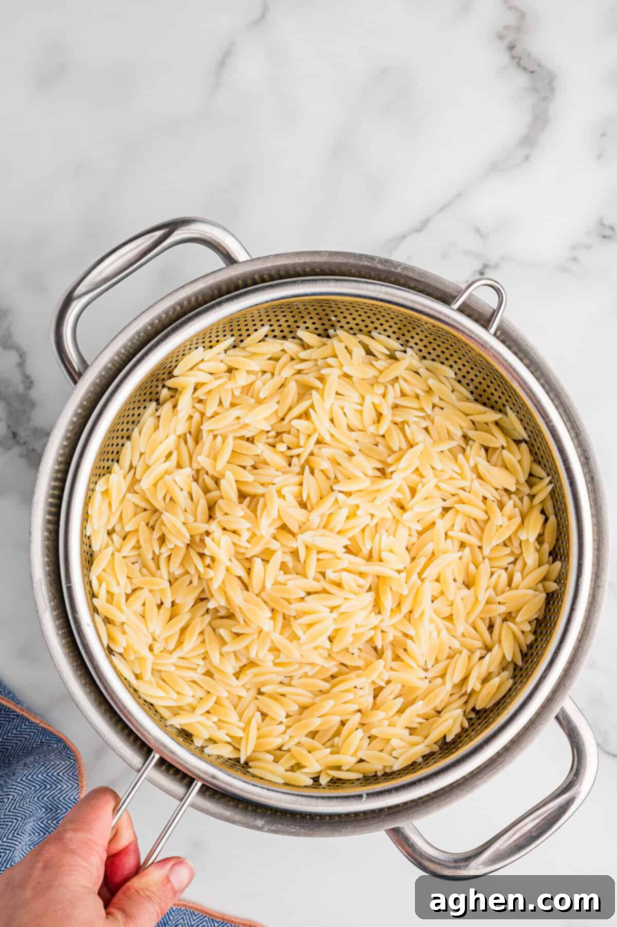Cooked orzo pasta draining in a metal colander over a pot.