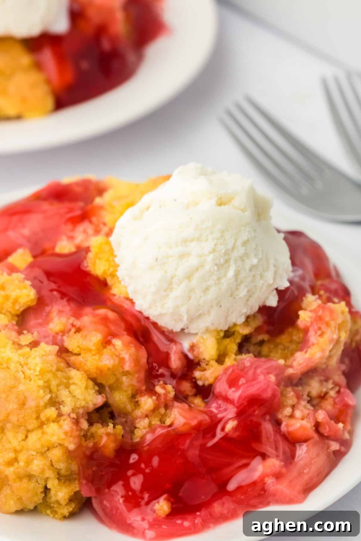 Easy Rhubarb Dump Cake 2 Rhubarb dump cake on a plate, topped with a round scoop of vanilla ice cream. The golden cake crumbles blend with the vibrant red filling beneath, ready to be enjoyed.