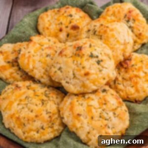 Fluffy Cheddar Biscuits 9 Pile of golden, herb-topped cheddar drop biscuits cheddar drop biscuits on a green cloth.