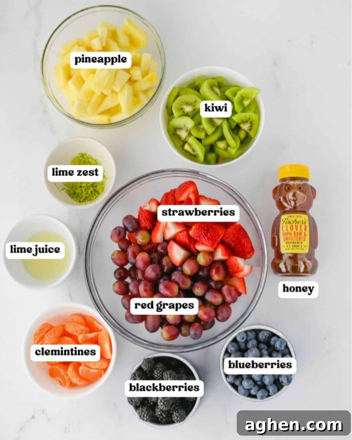 Fruit salad ingredients including pineapple, kiwi, strawberries, red grapes, blueberries, blackberries, clementines, lime zest, lime juice, and honey.