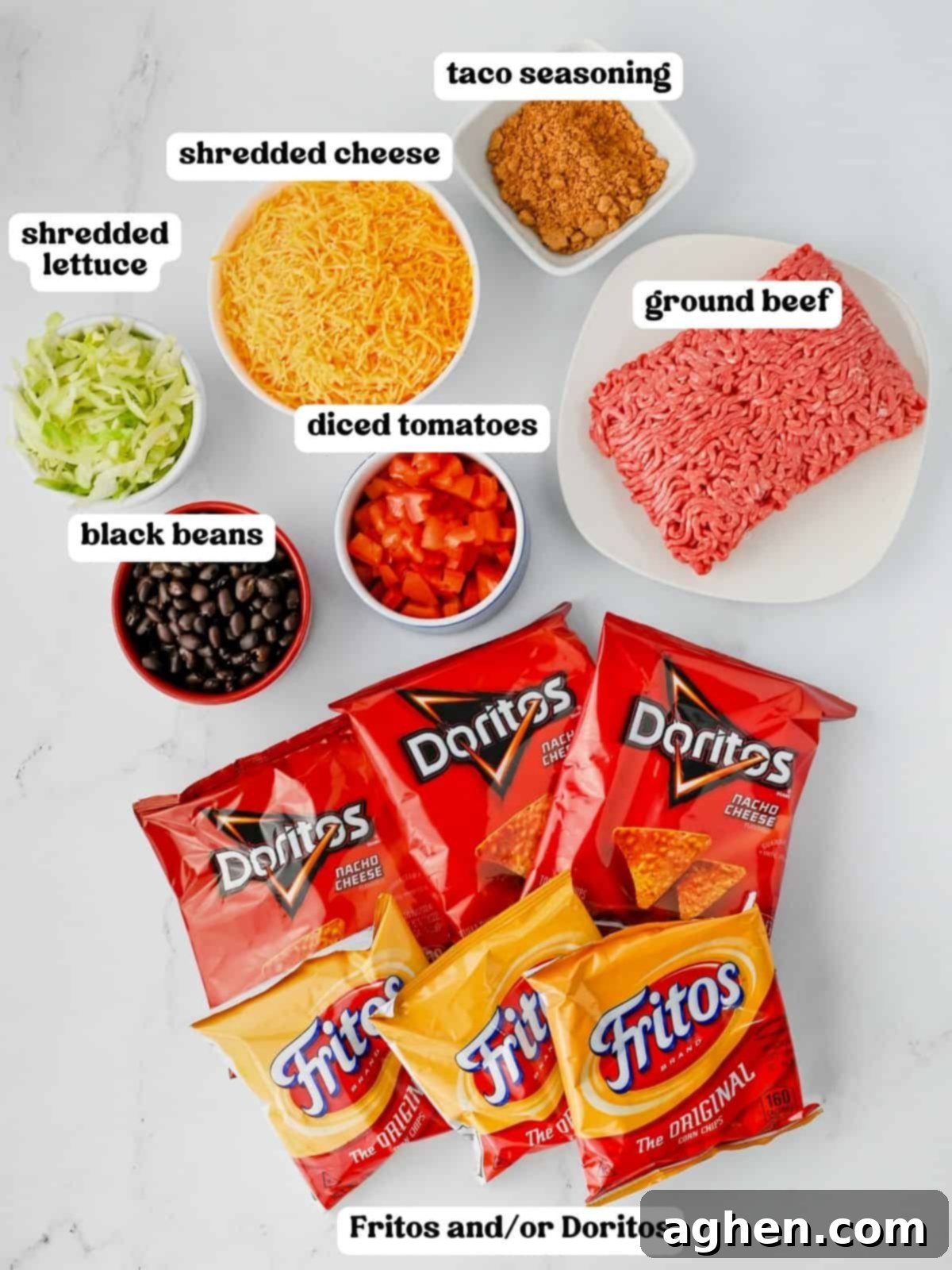 A colorful array of walking taco ingredients, including various small chip bags, a bowl of raw ground beef, taco seasoning, shredded cheese, fresh lettuce, black beans, and diced tomatoes, ready for assembly.