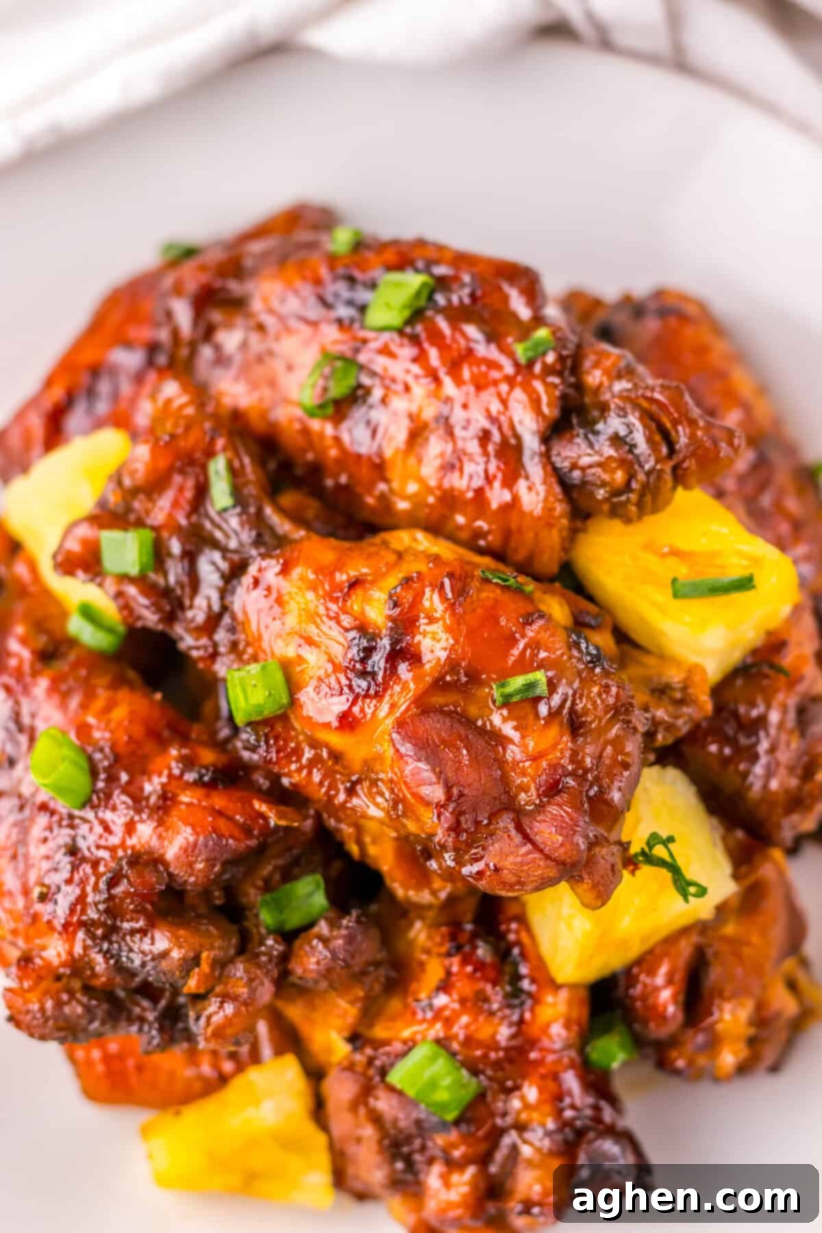 Close-up of glazed crockpot Hawaiian chicken wings, topped with bright yellow pineapple chunks and sprinkled with chopped green scallions.