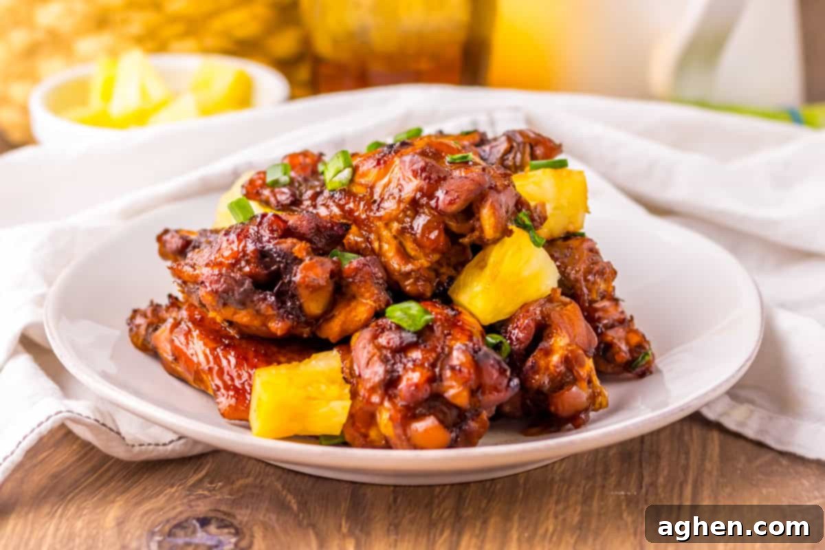 Hawaiian chicken wings on a white plate, featuring a glossy, dark glaze and garnished with pineapple chunks and chopped scallions.