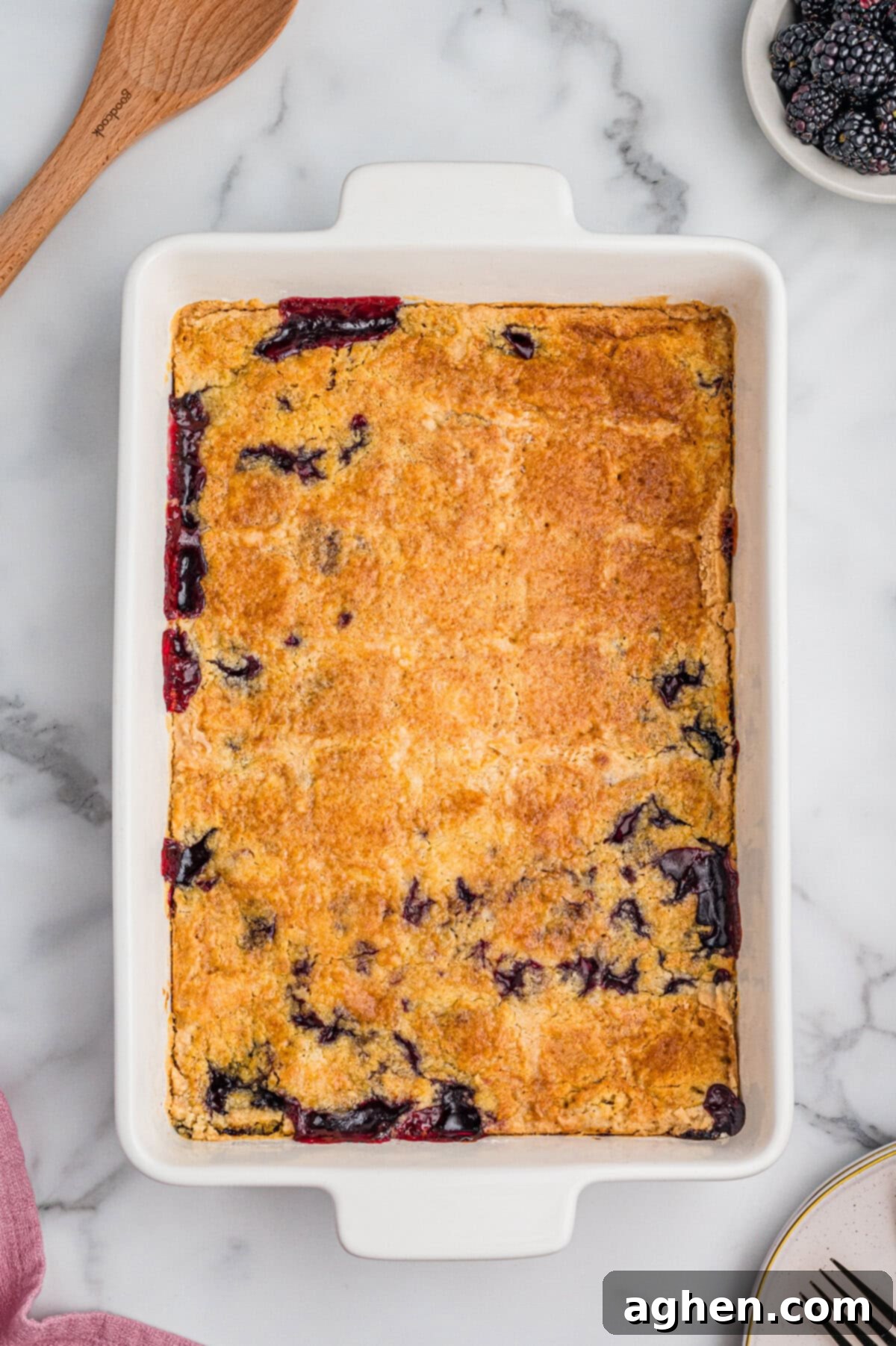 Blackberry dump cake in a 9x13 baking dish with a golden-brown top and patches of dark purple berry filling visible around the edges.