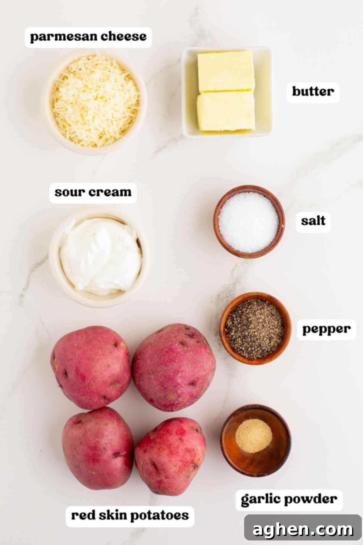 Overhead view of ingredients for mashed red potatoes with labels: Parmesan cheese, butter, sour cream, salt, pepper, garlic powder, and four whole red skin potatoes.