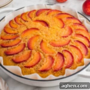Foolproof Peach Upside Down Delight 11 A peach upside-down cake in a parchment-lined white round dish. The top of the golden cake is decorated with arranged slices of fresh peach in a circular pattern.