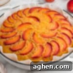 Foolproof Peach Upside Down Delight 12 A peach upside-down cake in a parchment-lined white round dish. The top of the golden cake is decorated with arranged slices of fresh peach in a circular pattern.