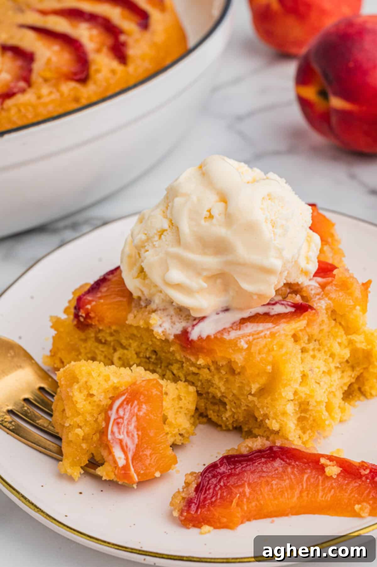 Foolproof Peach Upside Down Delight 9 A slice of golden peach upside-down cake with visible peach slices on top, served on a plate and topped with a scoop of vanilla ice cream. A fork with a bite of cake rests nearby.