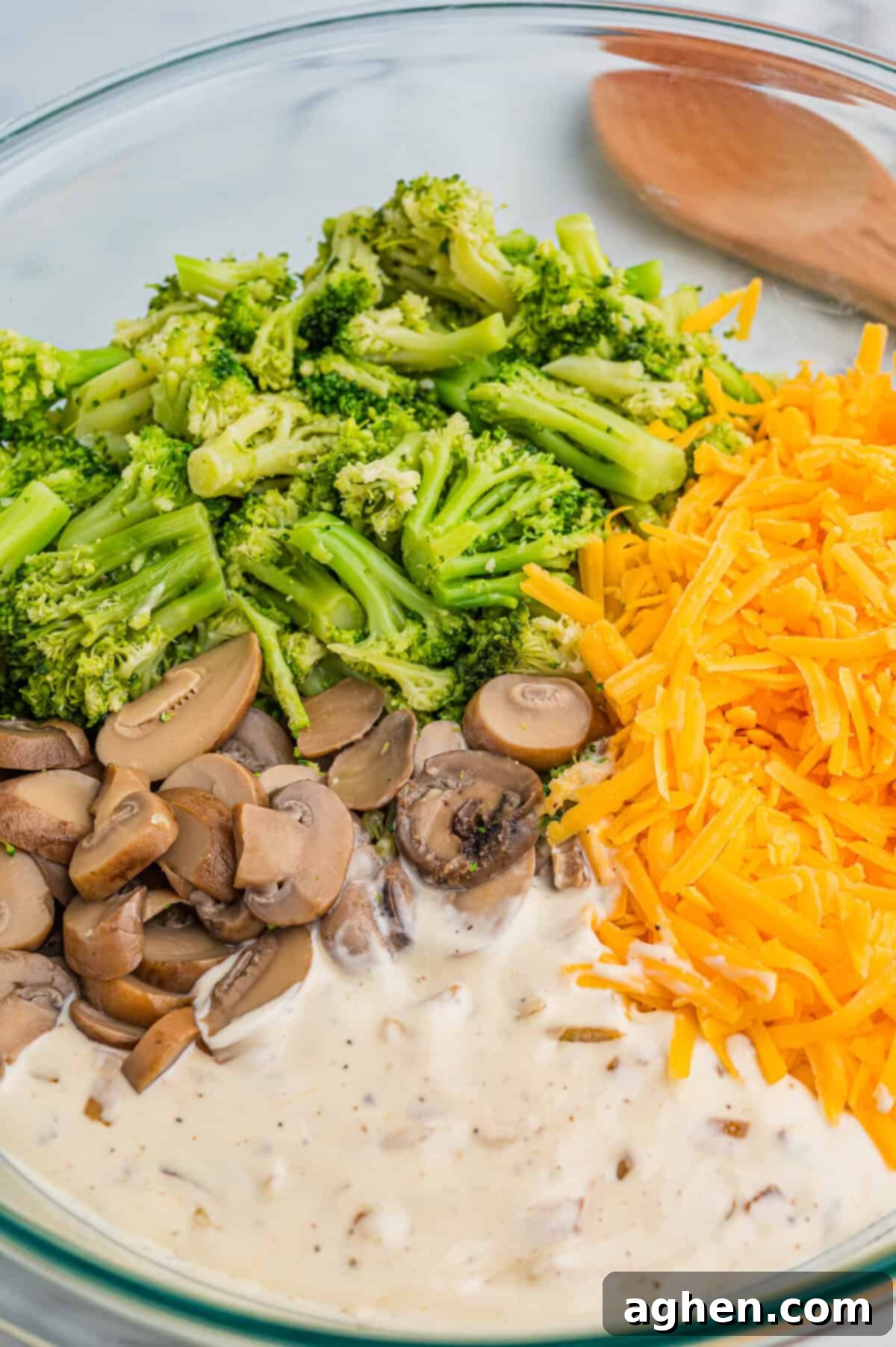 Cheesy Broccoli Delight 3 Mixing bowl containing bright green broccoli florets, sliced mushrooms, shredded cheddar cheese, and creamy mushroom soup, ready to be mixed for casserole.