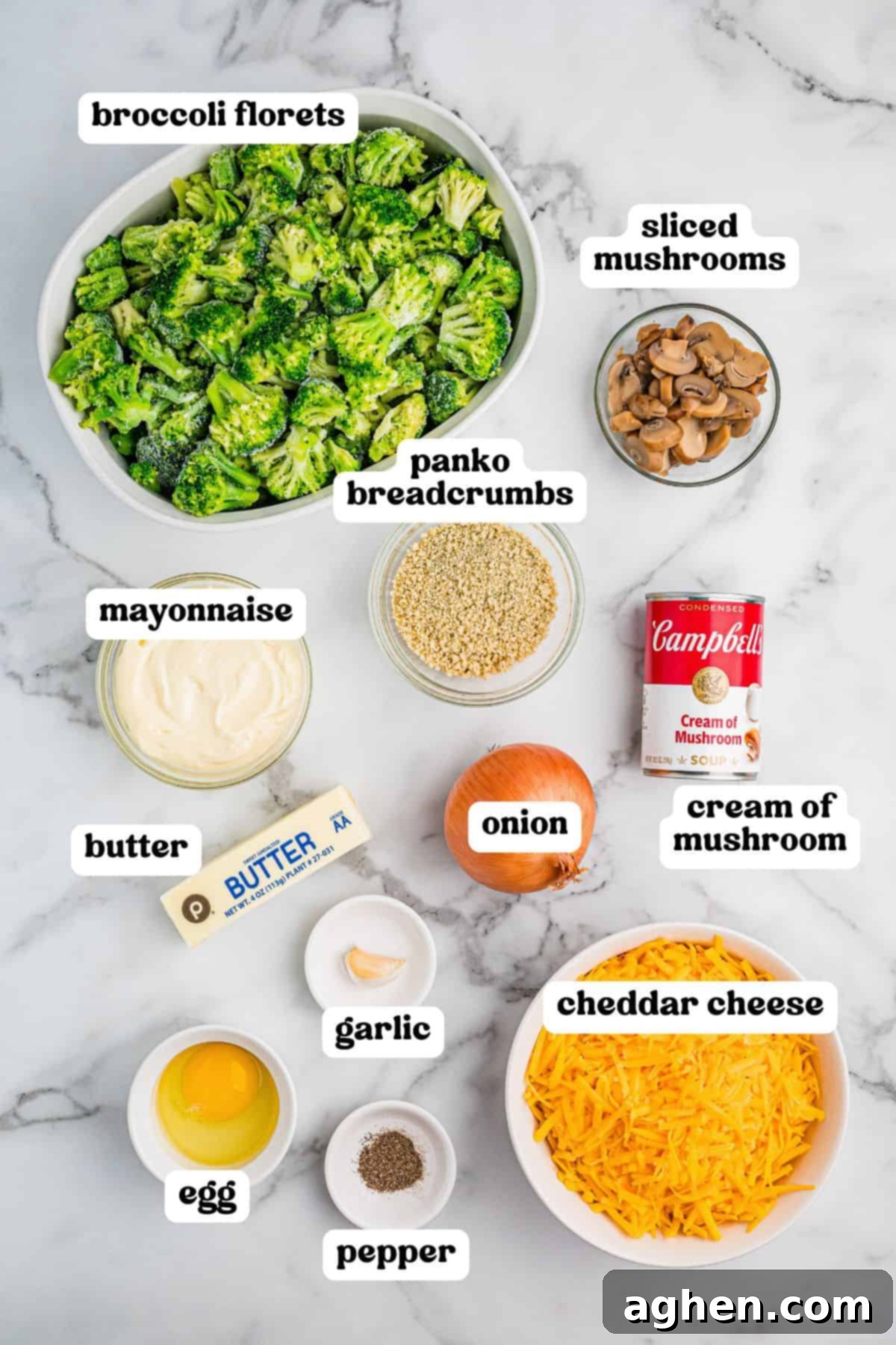 Cheesy Broccoli Delight 4 Overhead view of labeled ingredients for broccoli casserole including broccoli florets, sliced mushrooms, panko breadcrumbs, mayonnaise, butter, onion, cream of mushroom soup, garlic, egg, pepper, and shredded cheddar cheese.