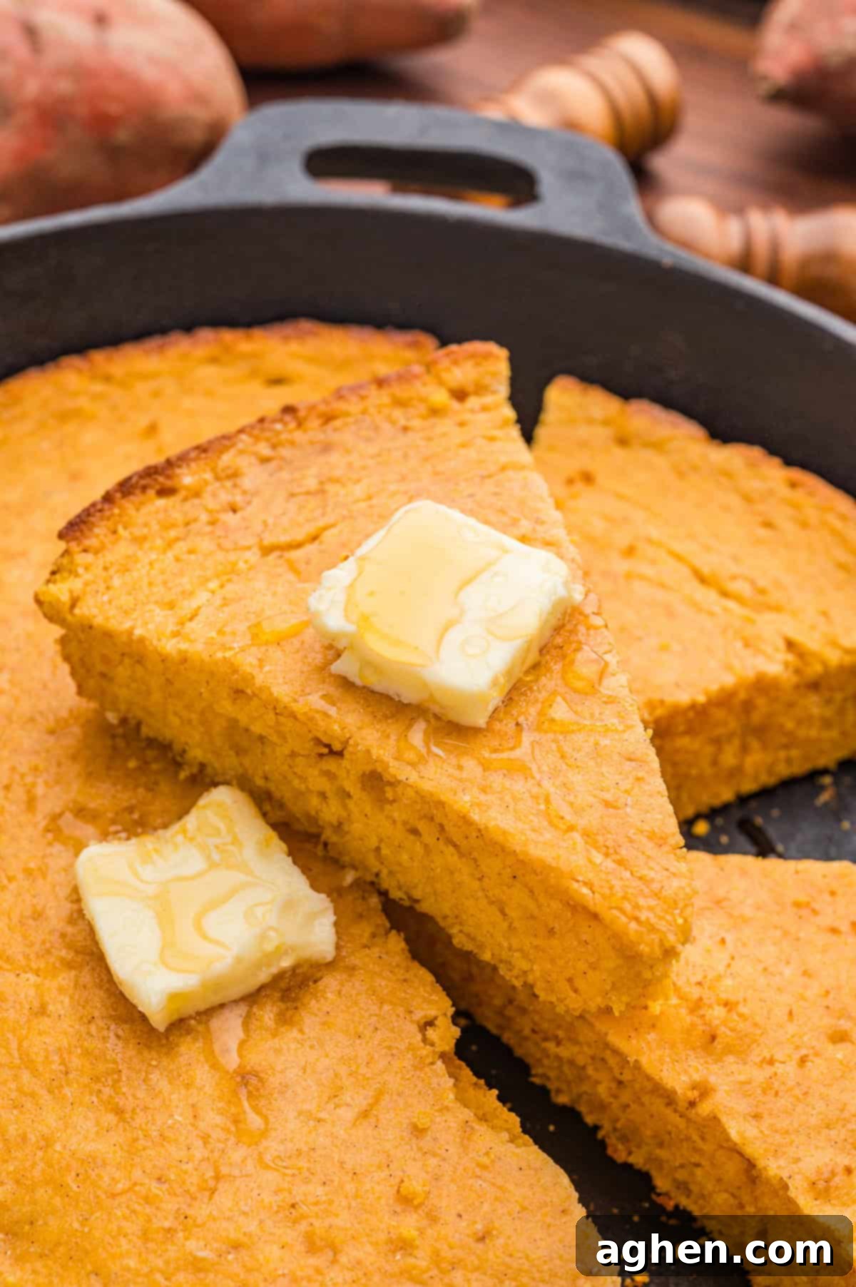 Several slices of sweet potato cornbread in a cast iron skillet with melting butter and honey drizzled on top, a true fall delight.