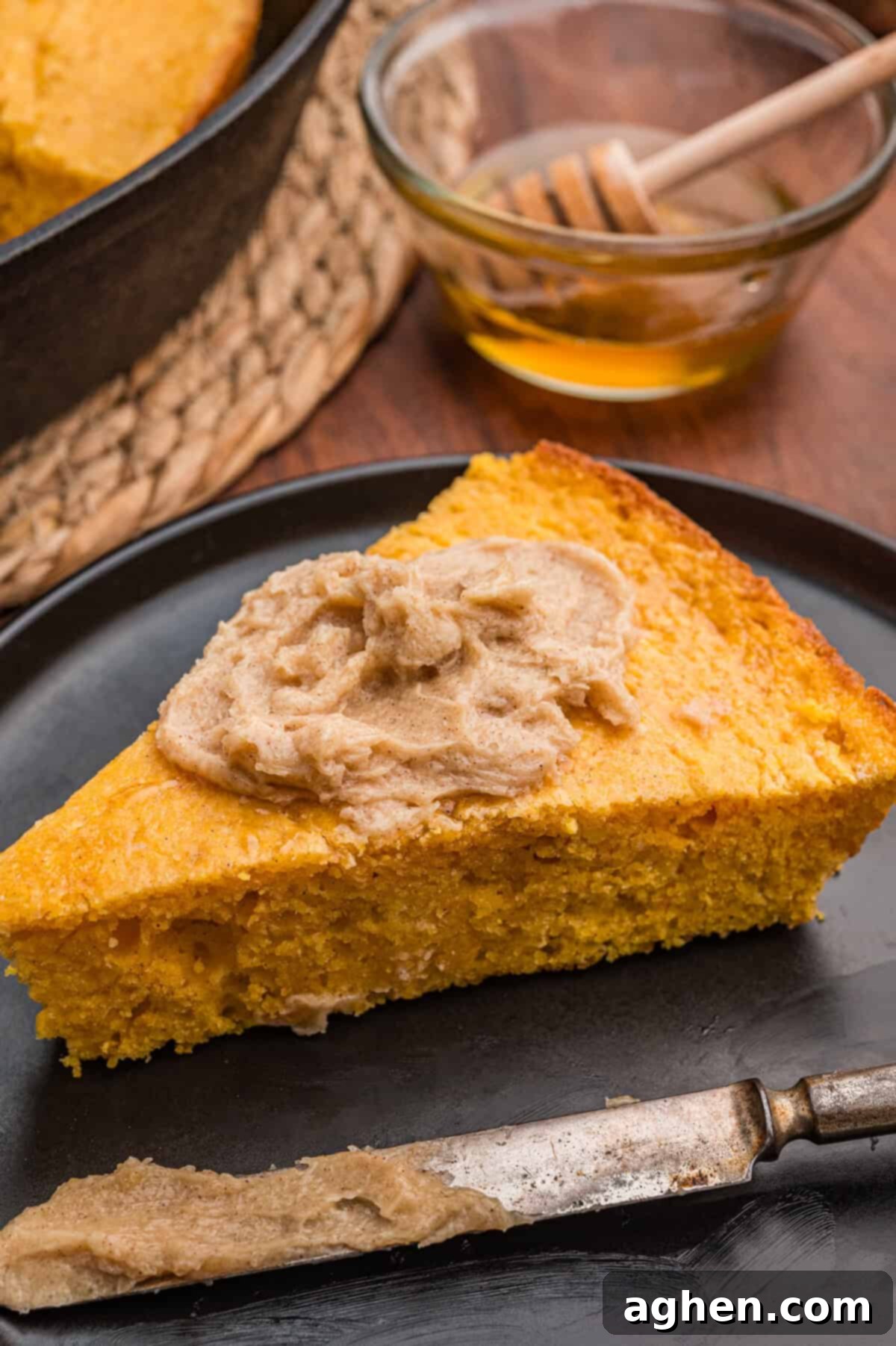Slice of sweet potato cornbread generously topped with creamy cinnamon butter spread on a sleek black plate, ready to be enjoyed.
