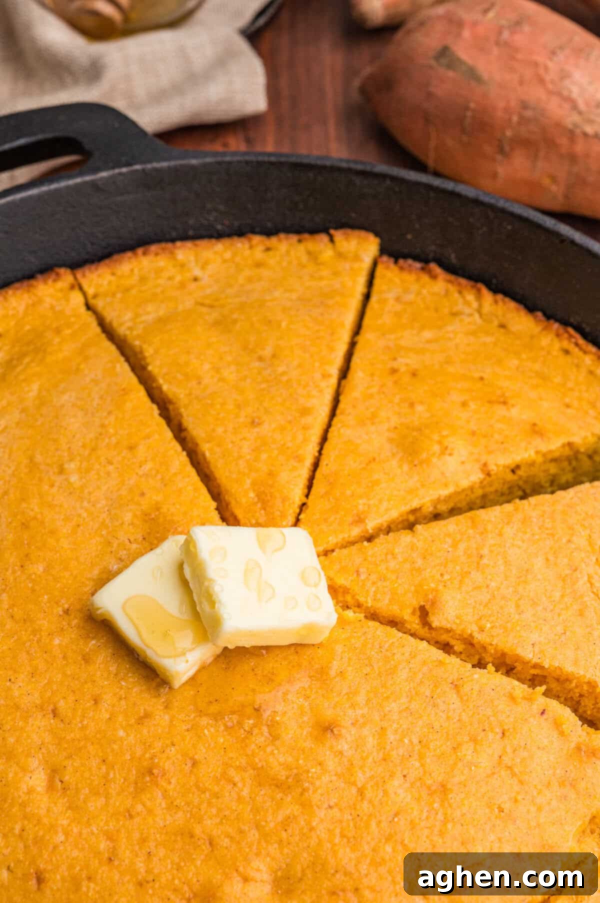 Close-up of golden-brown sweet potato cornbread wedges, glistening with melted butter and drizzled honey, highlighting its inviting texture.