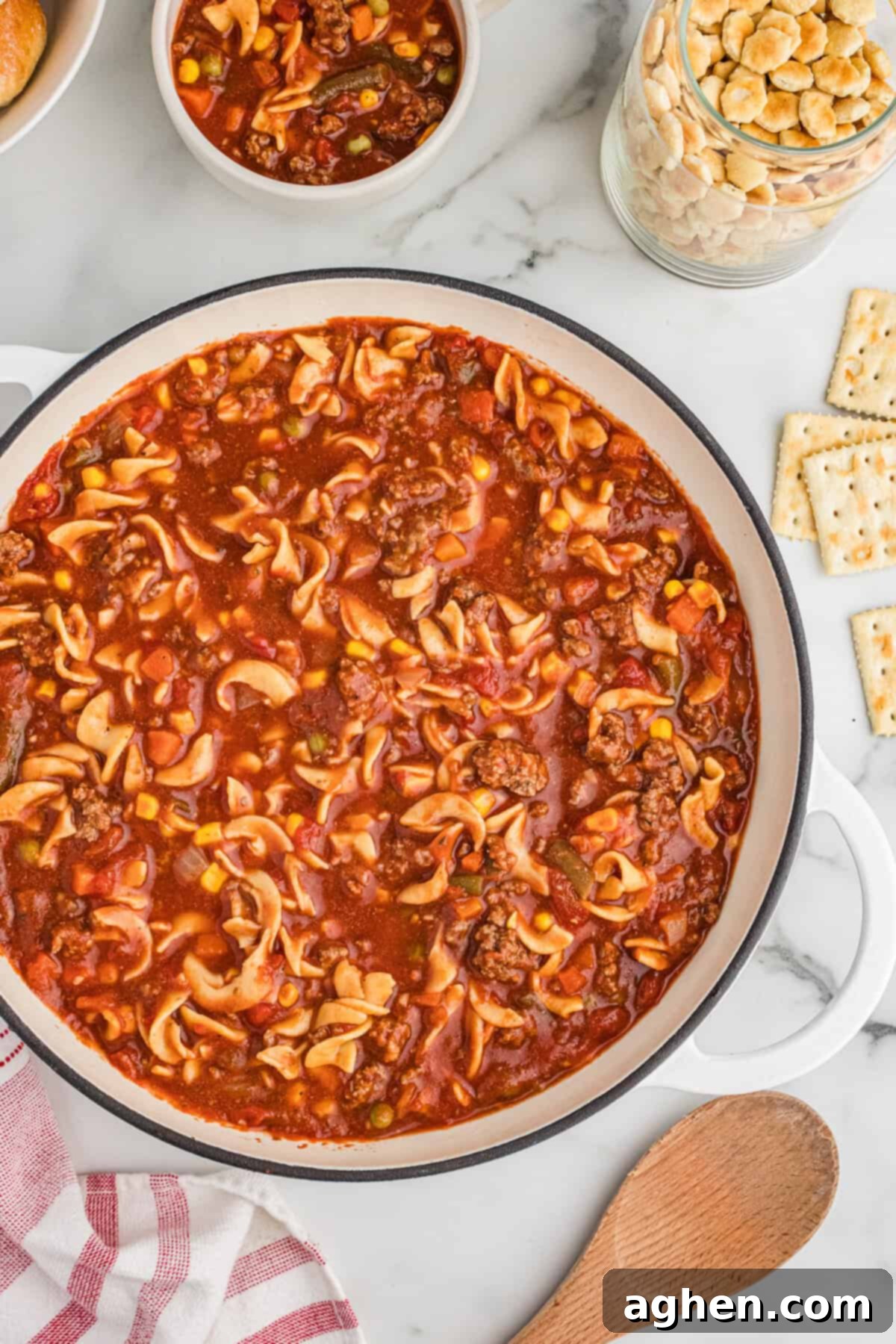 Overhead view of a large pot of hamburger noodle soup with ground beef, egg noodles, vegetables, and a tomato-based broth.