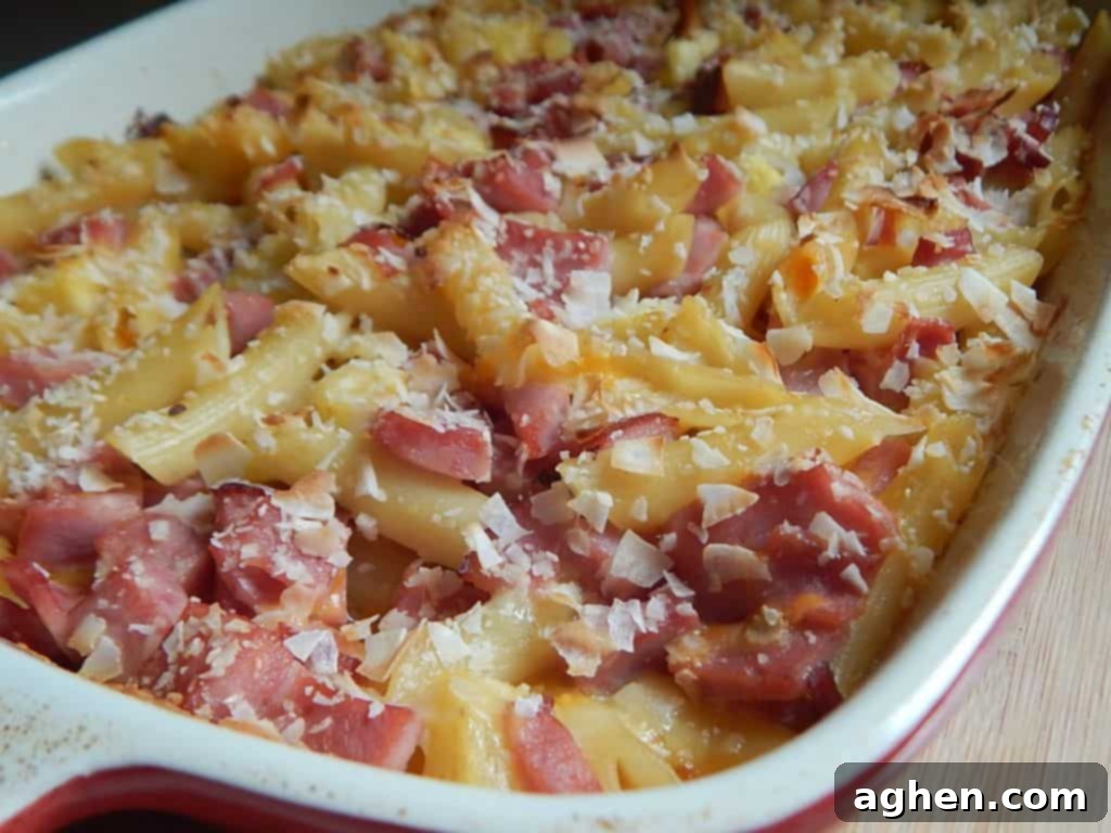 Island Paradise Pasta Bake 2 A delicious Hawaiian pasta bake, featuring penne, ham, and pineapple, served in a large casserole dish, with a golden, cheesy, and coconut-flaked topping.