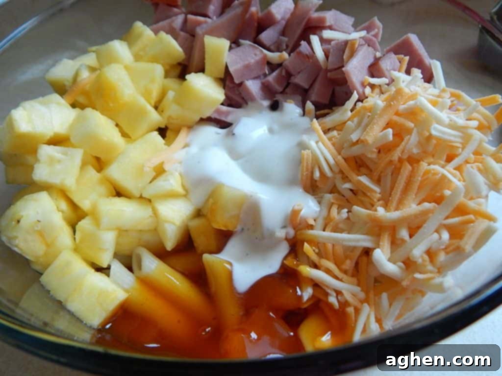 Island Paradise Pasta Bake 5 A selection of raw ingredients for Hawaiian pasta bake, including penne, diced ham, fresh pineapple, ranch dressing, and broth, laid out on a counter.