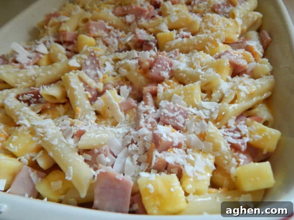 Island Paradise Pasta Bake 6 Hands mixing cooked penne pasta with diced ham and chopped fresh pineapple in a large clear bowl.