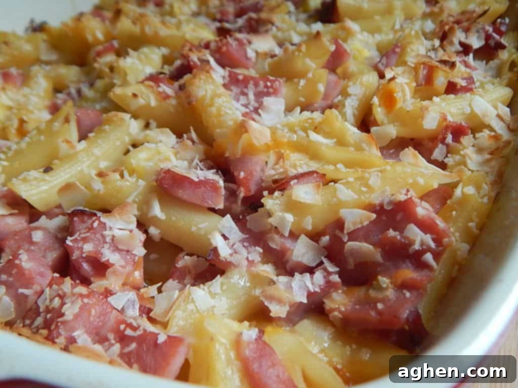 Island Paradise Pasta Bake 7 The Hawaiian pasta bake mixture in a glass casserole dish, topped with shredded cheese and unsweetened coconut flakes, ready for baking.