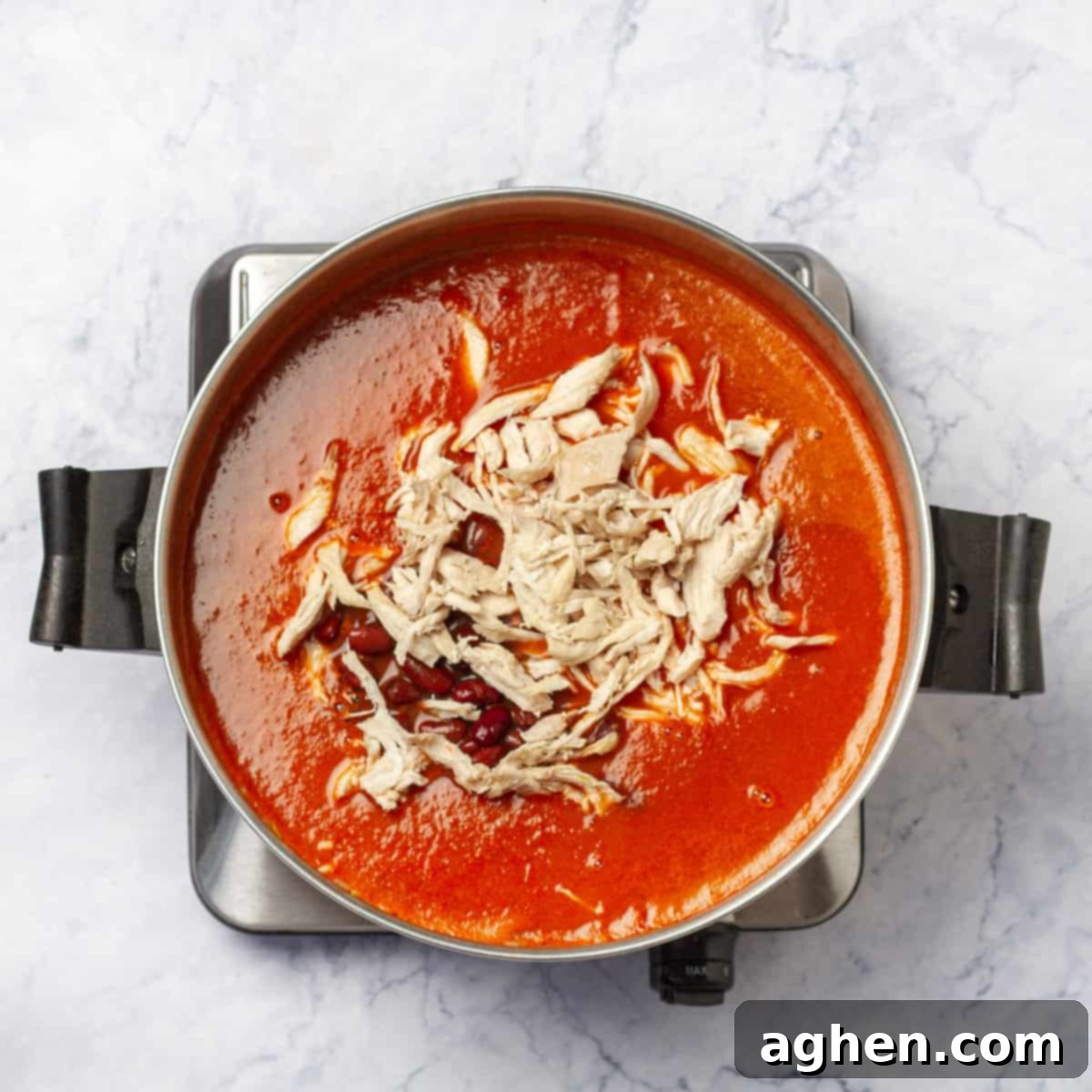 Wholesome Chicken Enchilada Soup 6 Tender shredded chicken pieces and dark red kidney beans being gently stirred into the rich, simmering soup, which already contains broth and vegetables, combining all the main ingredients for a hearty meal.