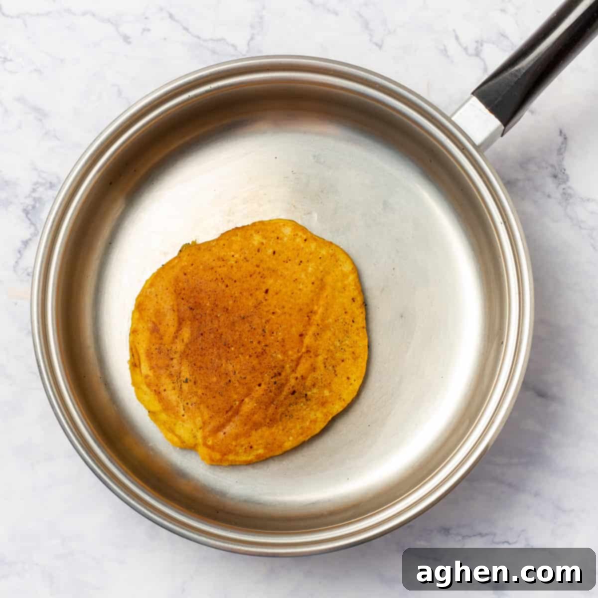 Fall Mornings Deserve These Irresistible Pumpkin Pancakes 6 A healthy pumpkin pancake cooking on a hot frying pan, showing the golden-brown bottom and bubbling surface, ready to be flipped for a perfect finish.
