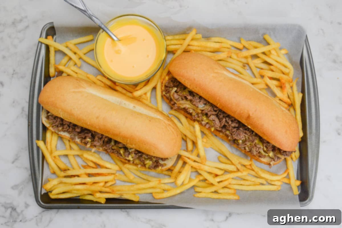 Make The Perfect Blackstone Philly Cheesesteak Every Time 10 Blackstone Philly Cheesesteaks on a tray with french fries and cheese sauce, ready to serve.