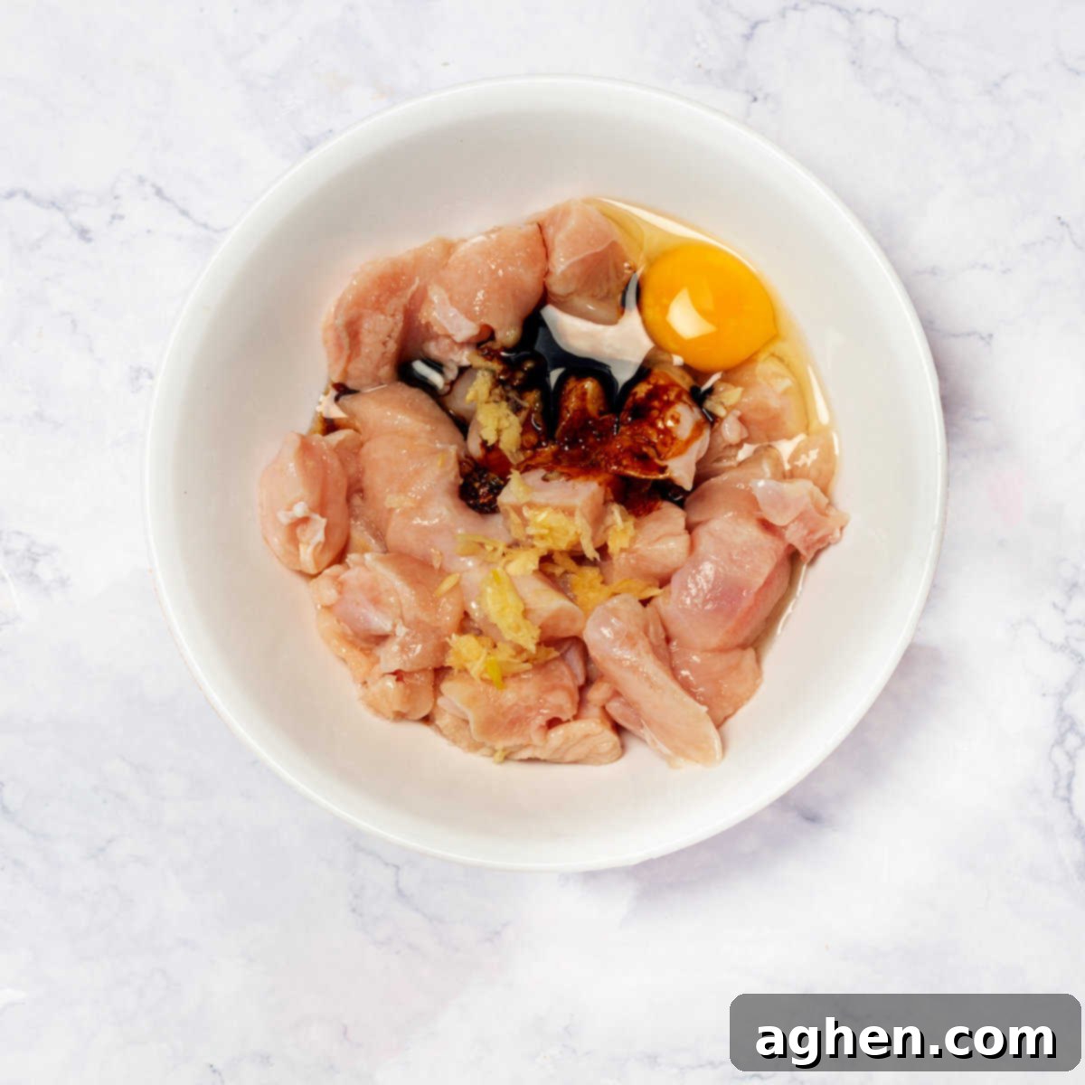 Lightened-Up Weight Watchers Orange Chicken 4 Chicken cubes marinating in a bowl with garlic, soy sauce, egg, and pepper.