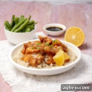Healthy Orange Chicken served with lemon and a bowl of beans, garnished with fresh herbs.