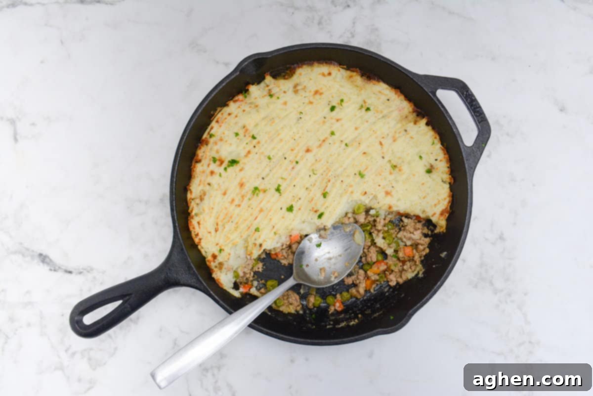 Weight Watchers' Timeless Ground Turkey Shepherd's Pie 10 The cooked Turkey Shepherd's Pie with a scoop taken out. A silver serving spoon sits inside the skillet where small amounts of vegetables and meat peek out from under the potatoes.