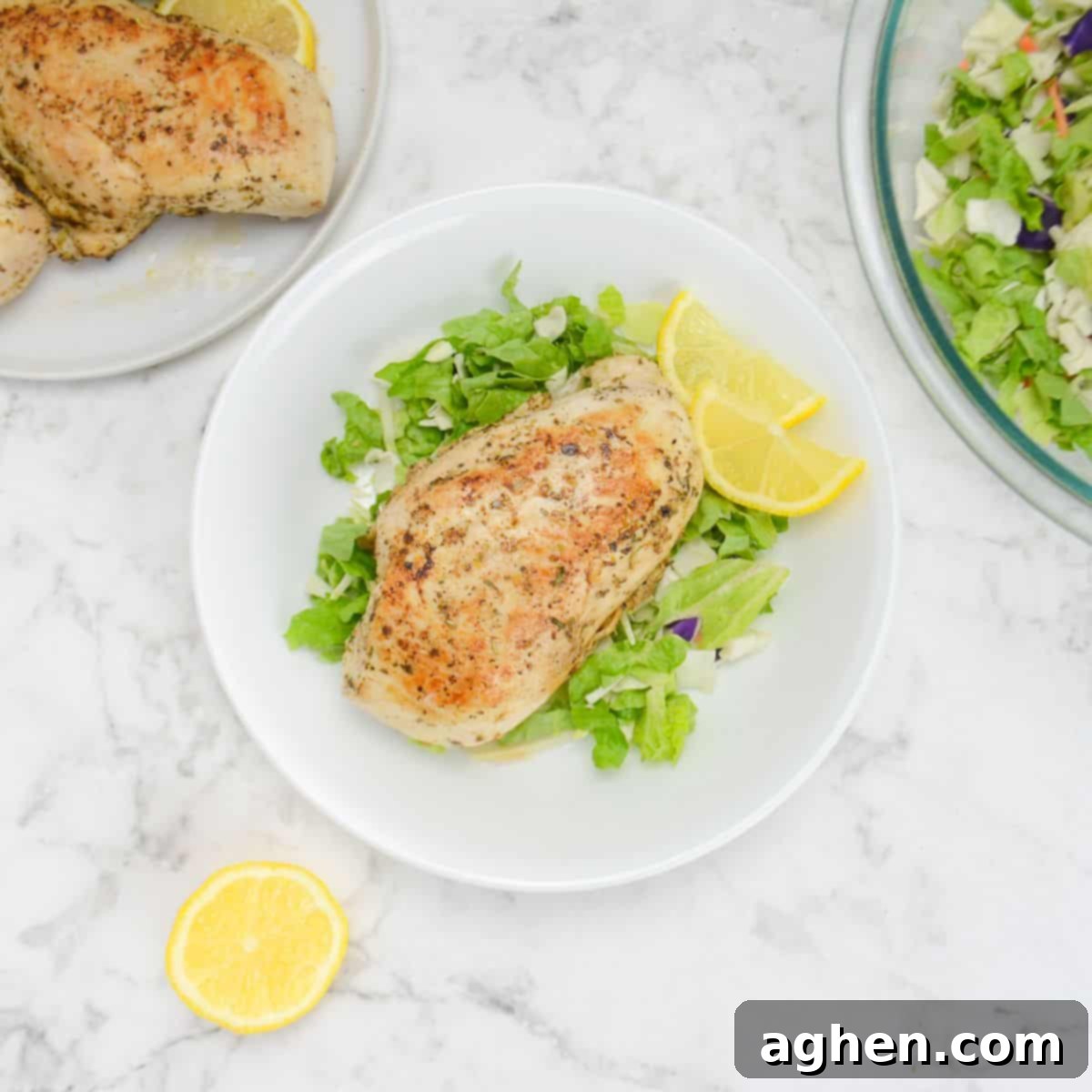 The Secret to Juicy Chicken Breasts on Your Blackstone 2 A white plate with chopped romaine lettuce. A cooked chicken breast sits in the middle of the plate with two lemon wedges to the side. A bowl of salad, plate of chicken and a cut lemon sit to the side of the plate.