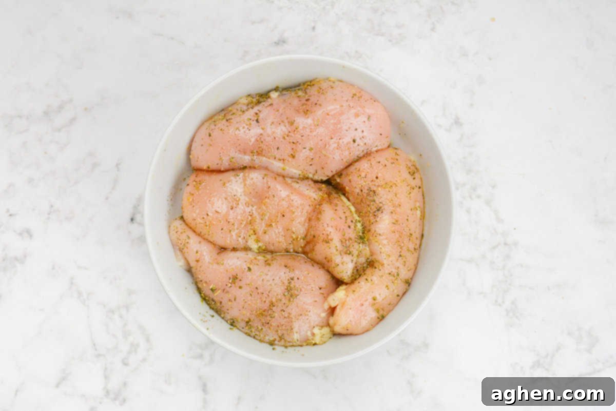 The Secret to Juicy Chicken Breasts on Your Blackstone 5 A large white bowl containing raw chicken that is covered in olive oil and seasoning