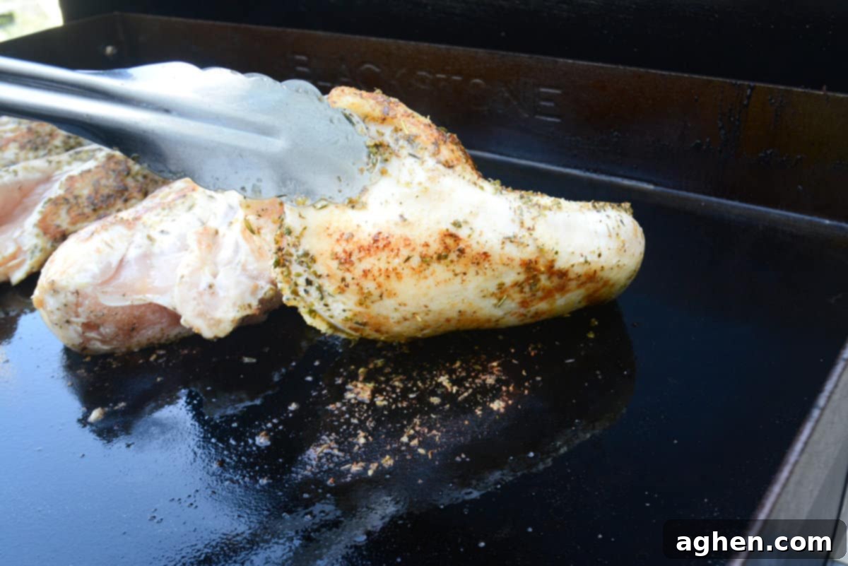 The Secret to Juicy Chicken Breasts on Your Blackstone 7 Silver metal tongs lift one edge of a single piece of chicken breast showing how it lifts easily