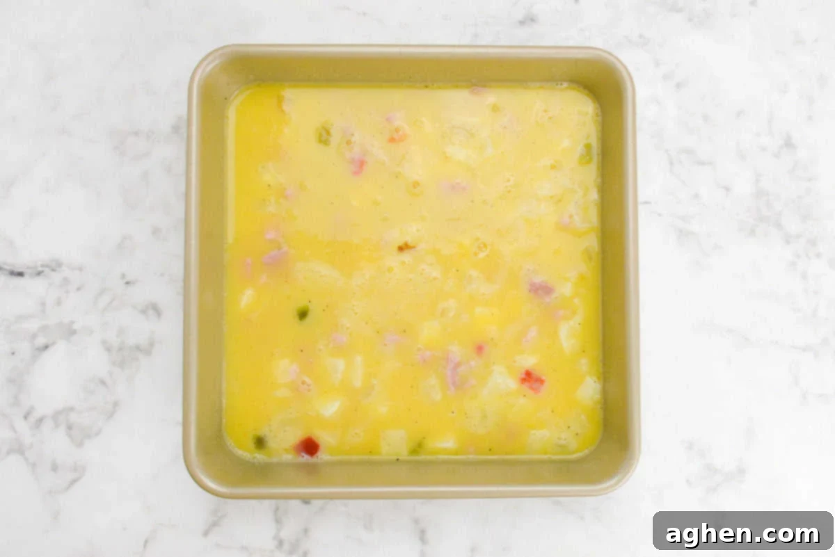 Smart Start Breakfast Bake 8 A gleaming gold baking pan is now filled with the uncooked egg mixture for the breakfast casserole, its surface ready for the final toppings before baking.