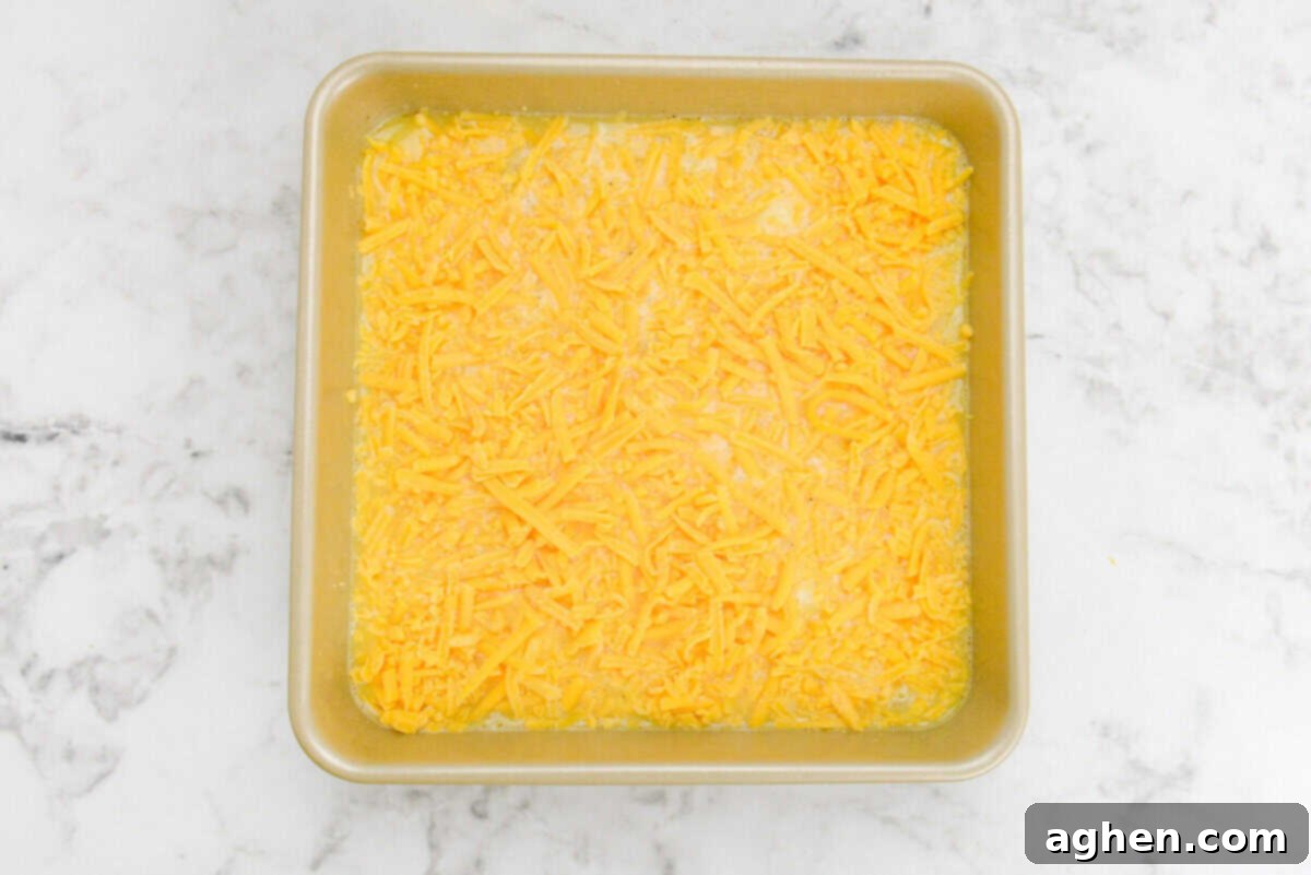 Smart Start Breakfast Bake 9 An unbaked but fully assembled breakfast casserole, beautifully topped with a layer of shredded cheddar cheese, rests within a golden baking pan, poised for its transformation in the oven.