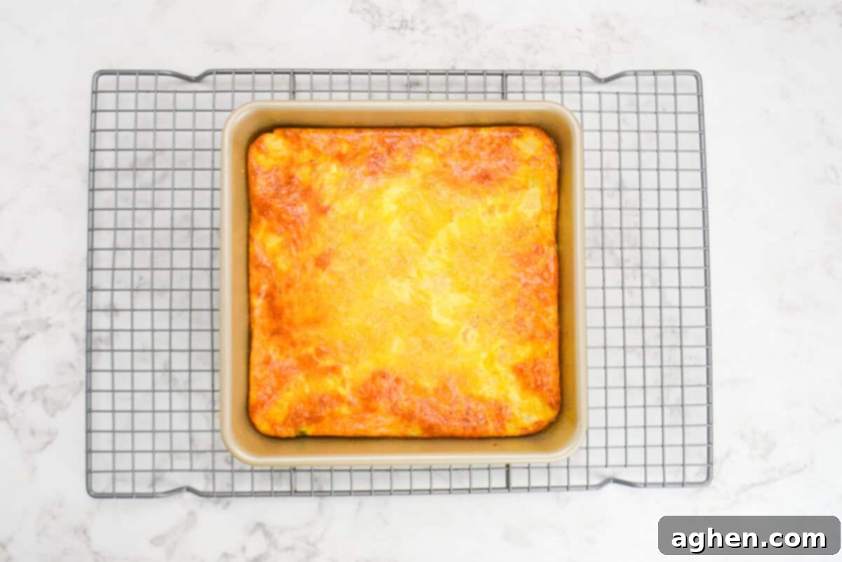Smart Start Breakfast Bake 10 The freshly baked breakfast casserole, with beautifully browned edges and a slightly lighter center, is still in its gold baking pan, cooling on a silver wire rack after being removed from the oven.