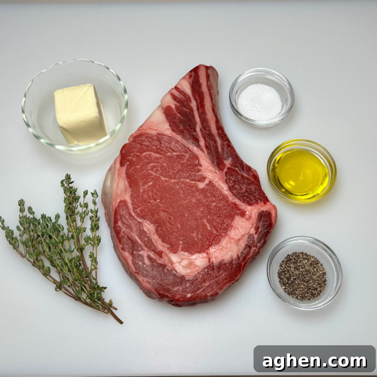 Mükemmel Biftek: Döküm Tavada Pişirmenin Püf Noktaları 3 Raw ribeye steak with seasoning, olive oil, butter, and thyme sprigs arranged around it on a wooden board.