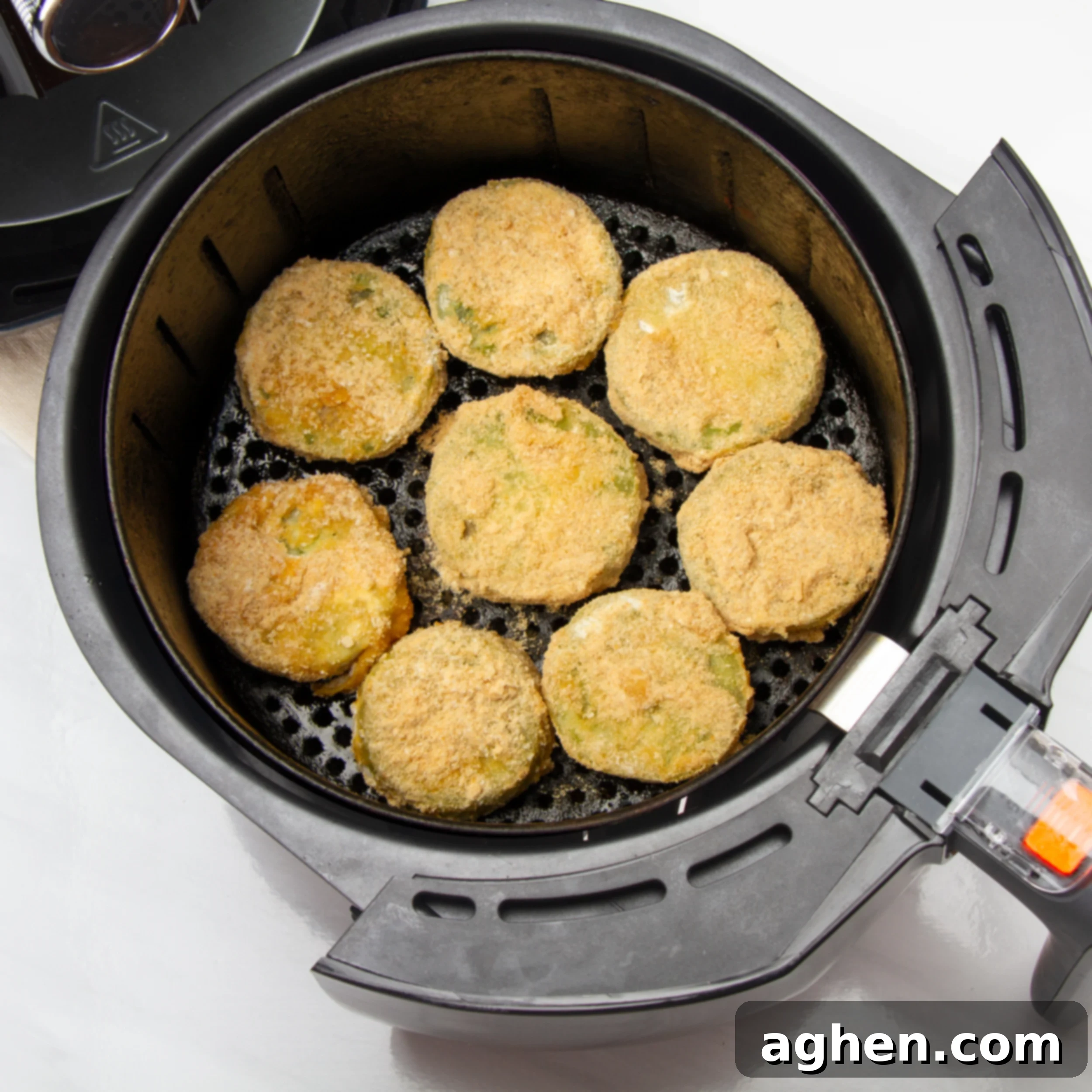 Golden Crispy Air-Fried Green Tomatoes 6 Breaded green tomatoes spread in a single layer in an air fryer basket.