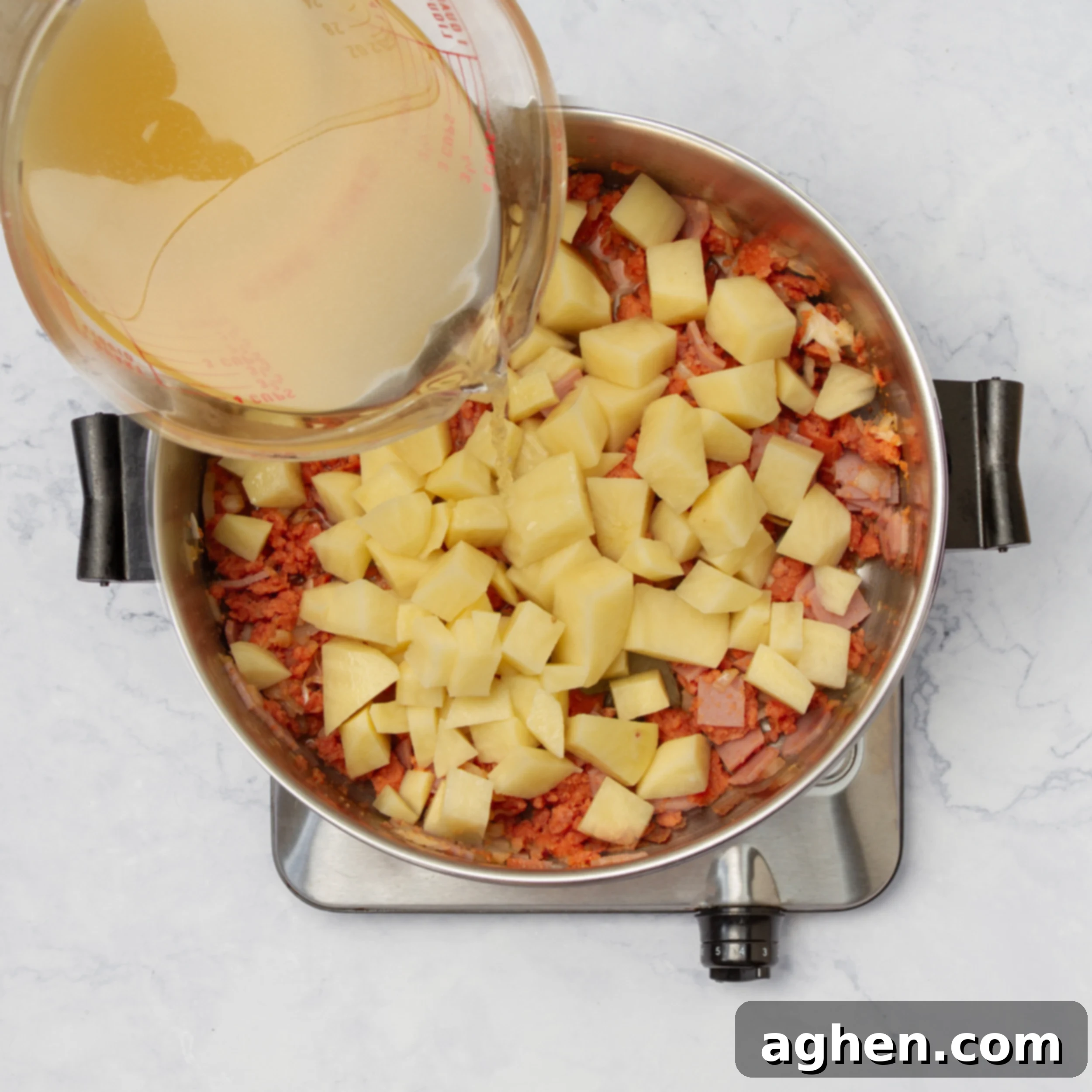 Mastering Olive Garden's Zuppa Toscana At Home 5 Potato cubes and broth being added to the sauteed meats and aromatics in a hot pot.
