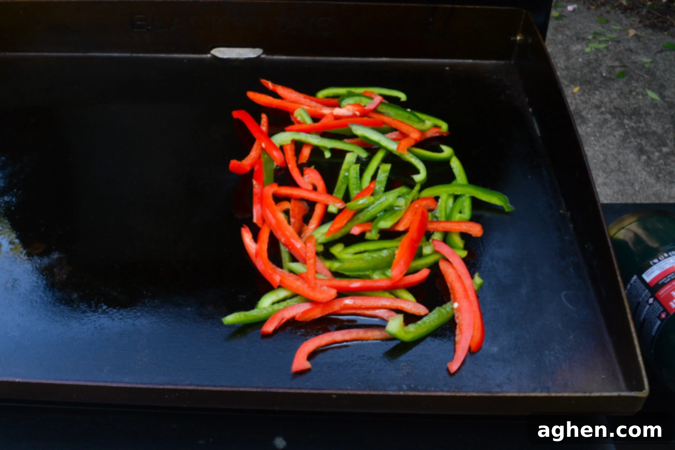 Blackstone Steak Quesadillas So Good They're Eaten Off the Griddle 4 sliced green and red bell peppers cooking in oil on a blackstone griddle.