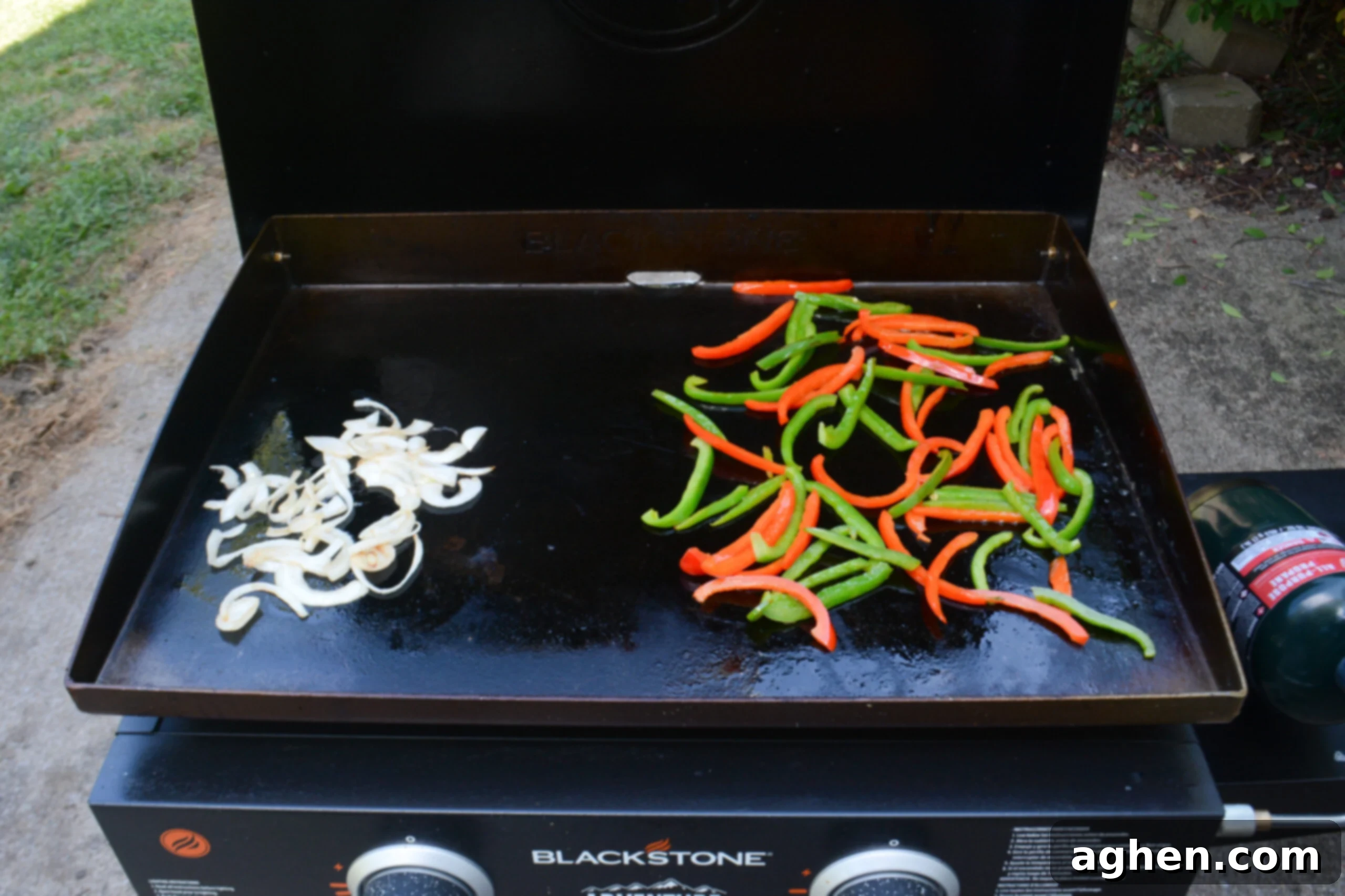 Blackstone Steak Quesadillas So Good They're Eaten Off the Griddle 5 sliced onions cooking on one side of a blackstone griddle and sliced green and red bell peppers cooking on the other side of the same griddle.